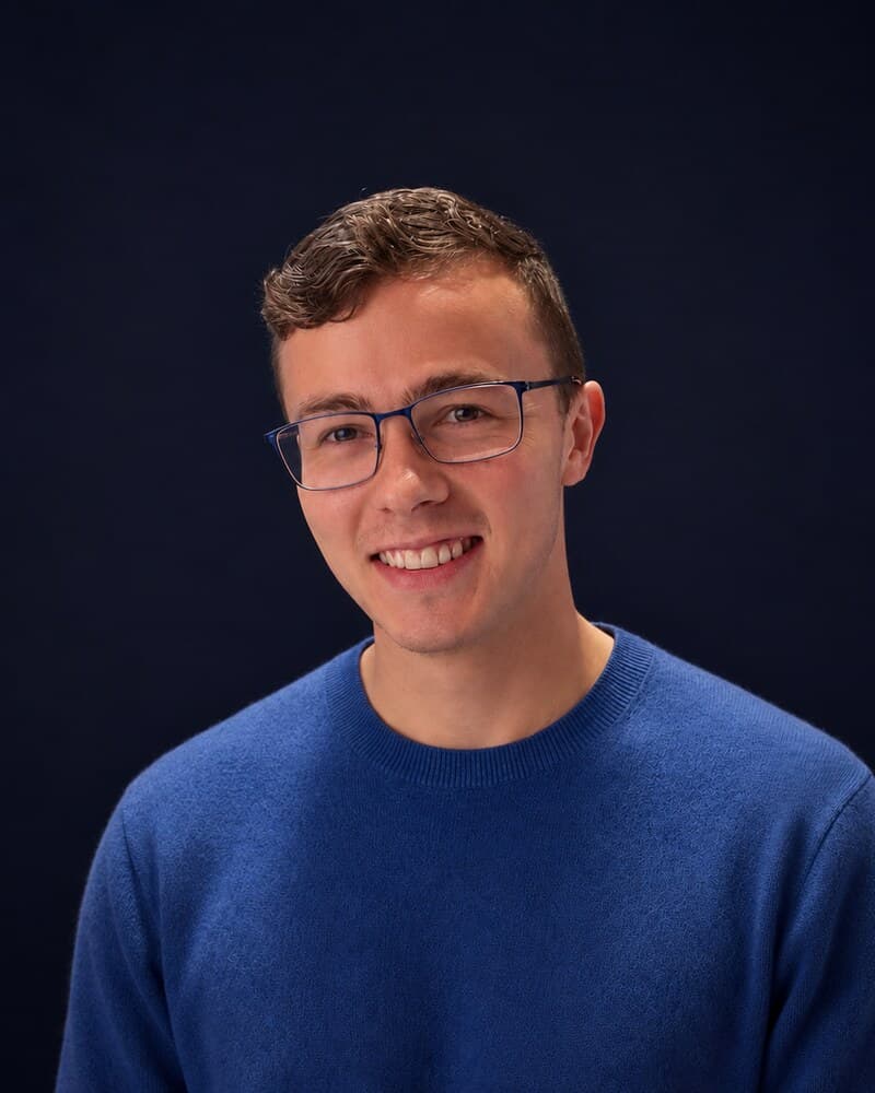 Angus Moore, founder of Made to Fit AI. Studio portrait in glasses and a blue jumper, smiling.